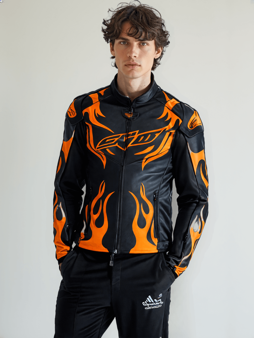Close-up of the front detailing on a black leather motorcycle jacket with orange flame accents and a stylish biker logo.